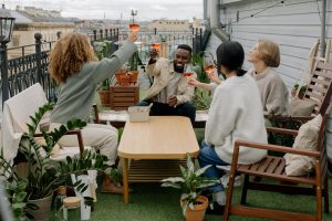 4 personas alzan una copa de vino rosado en la terraza del piso mas alto de un bloque, rostros felices, ocurre en una ciudad. Encuentro de meetup