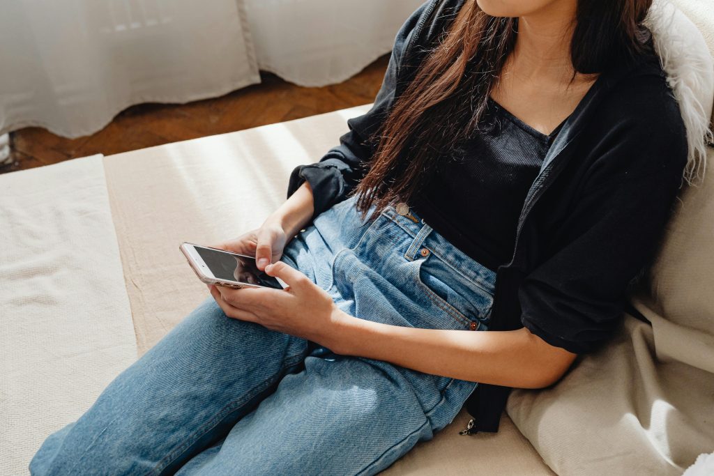 Una mujer joven sentada en un sofá usando un smartphone.